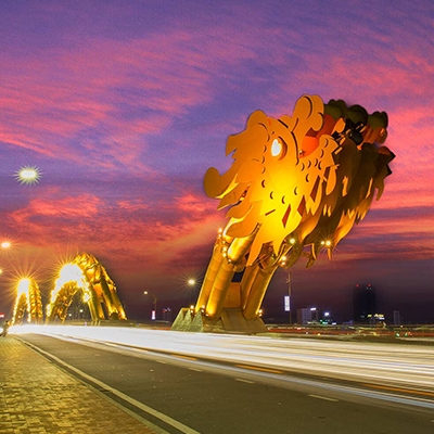 Cầu Rồng Đà Nẵng trên nền hoàng hôn, ánh sáng vàng rực rỡ nổi bật trên bầu trời tím.