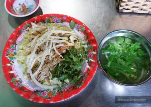 Cơm gà Hội An trên đĩa với thịt gà xé, hành tây, rau thơm và nước dùng bên cạnh.