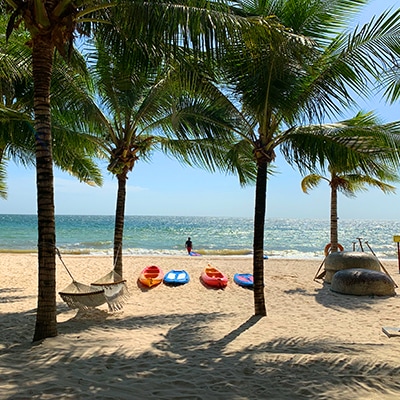 Bãi biển Phú Quốc với dừa xanh và thuyền kayak đa màu, người tắm biển ở xa.